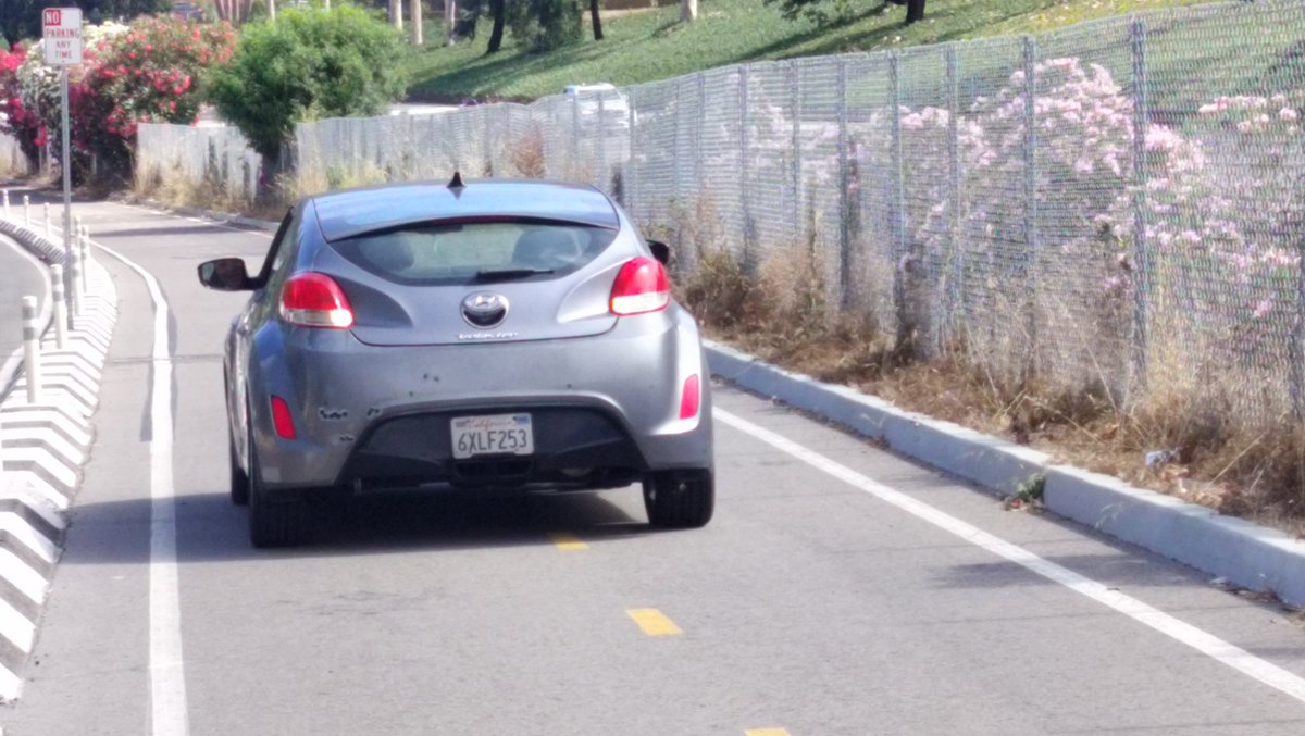 Car driving recklessly driving when cyclists are in a protected bike lane on Santa Fe Street between the brewery and campground in San Diego California