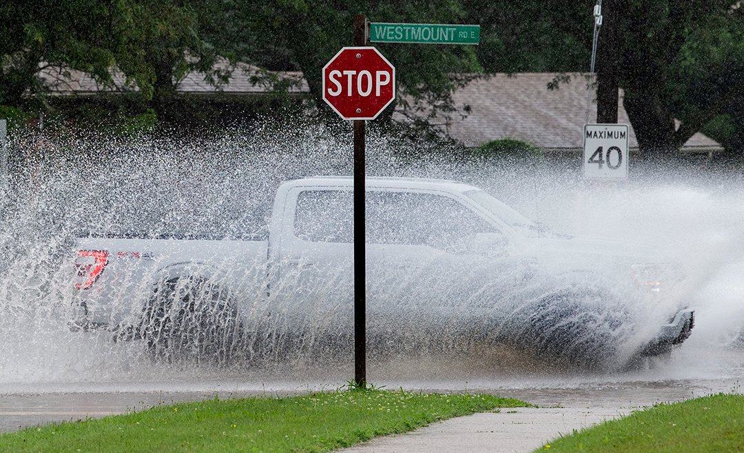 Vehicles kick up rooster tails of water as they drive through deep puddles on Westmount Road at Village Road in Kitchener, Tuesday, July 16, 2024. #onstorm