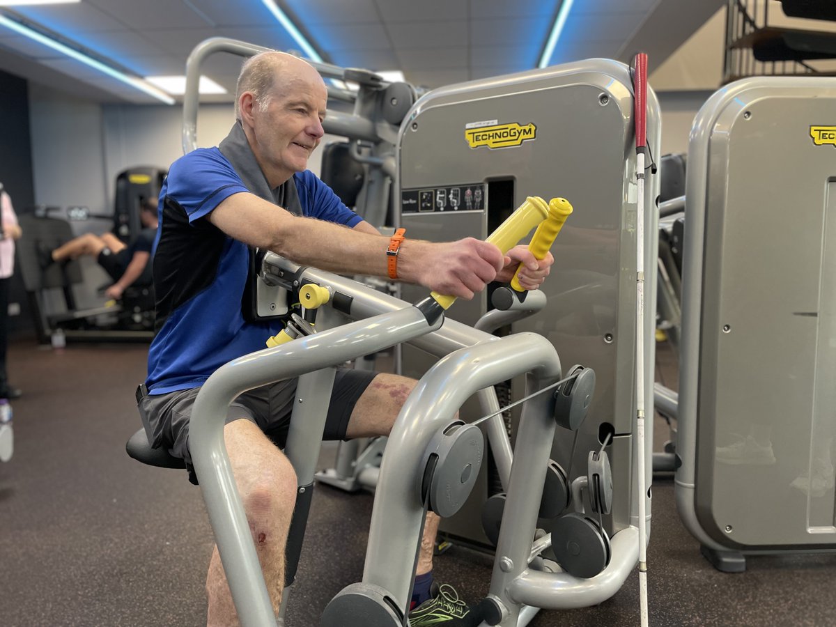 Glasgow Club member Raymond Ward using a low row back machine at Glasgow Club Tollcross gym. They have their arms out in front of them holding onto the handles of the machine.