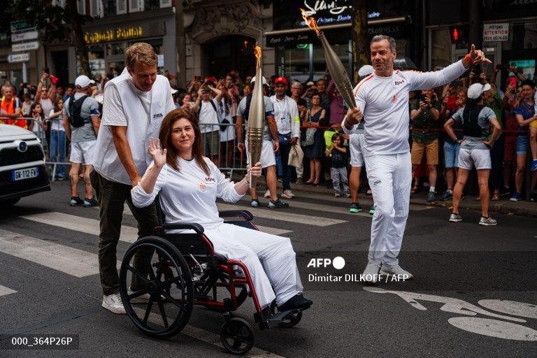 Agence France Presse (AFP) Lebanese photographer Christina Assi (C) helped by AFP video journalist Dylan Collins (L), waves after receiving the Olympic flame during the Olympic Torch Relay in Vincennes, ahead of the Paris 2024 Olympic Games. #OlympicGames 

📸Dimitar DILKOFF #AFP