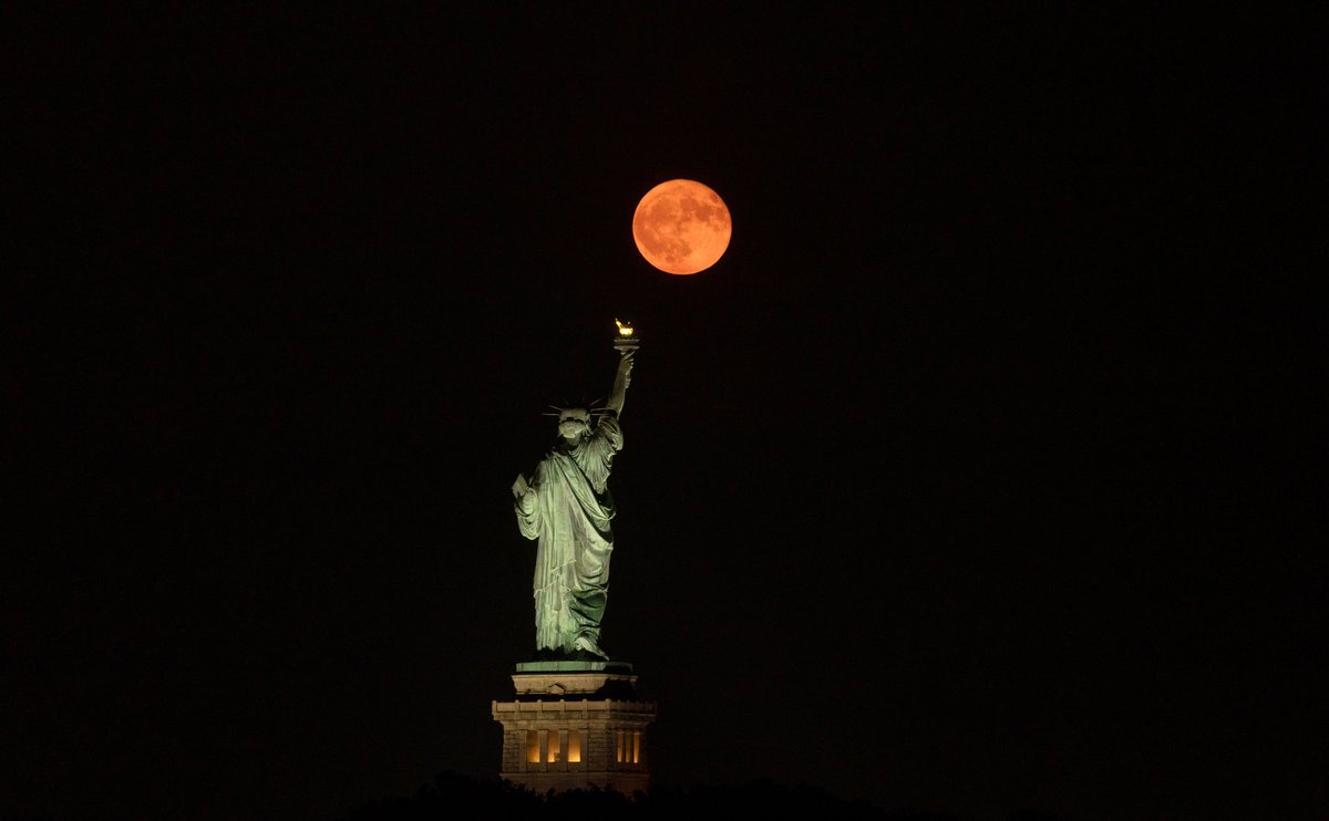 GaryHershorn's tweet image. The full Buck Moon rising behind the Statue of Liberty in New York City, Sunday evening.