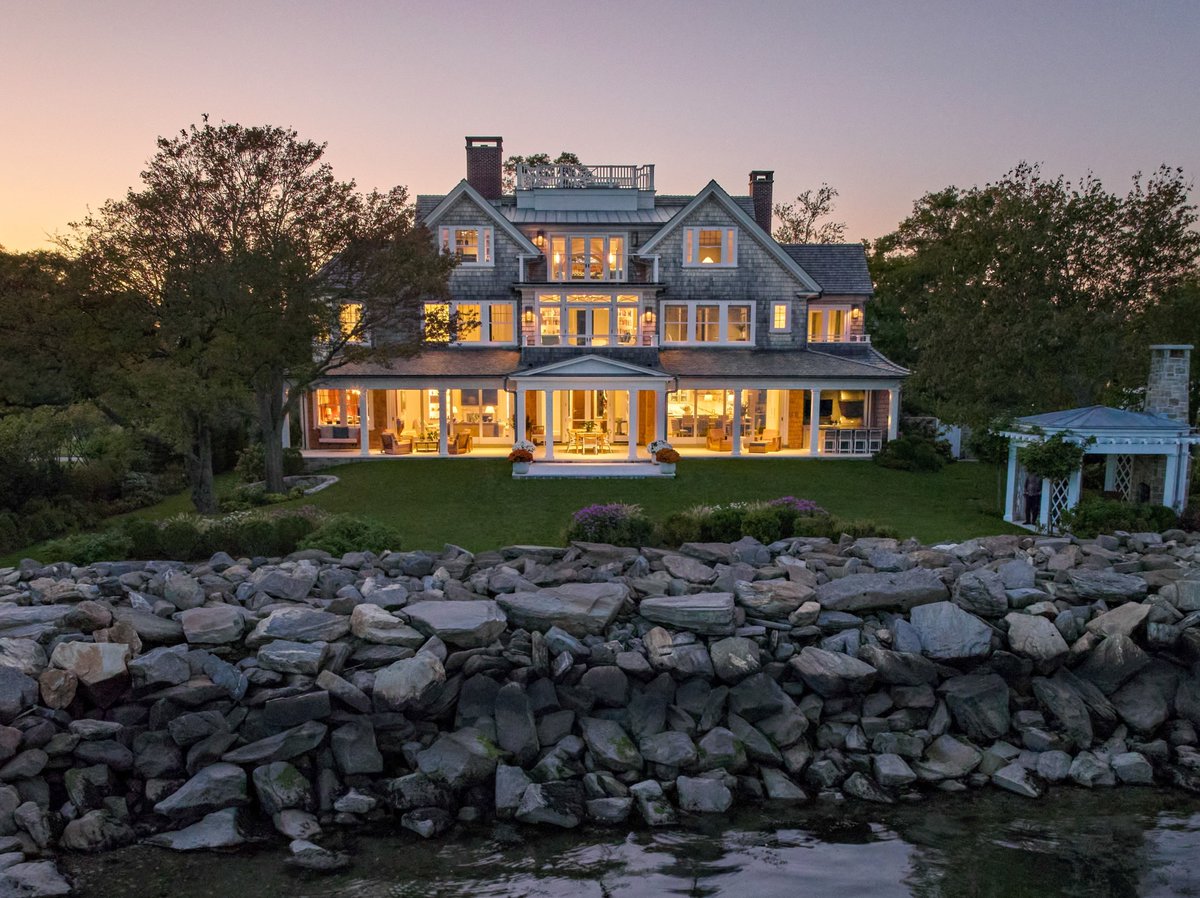 At our new Shorefront Shingle design, the rear porch runs the entire length of the home. Stacking sliding doors in the family room and kitchen open the first floor to the shorefront, blurring the line between interior and exterior. #luxuryhomes #homedesign #architecture