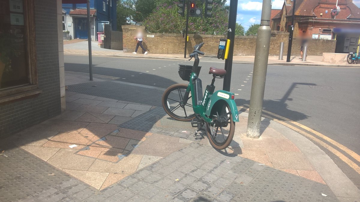 DocklessLondon's tweet photo. From last Wednesday. A Forest bike parked outside a café in Wandsworth, obstructing pedestrian crossings for all and with front and back wheel on elements of tactile pavement used by blind and visually impaired. #DocklessBikes #PavementsAreForPeople https://t.co/wPop9p6e16