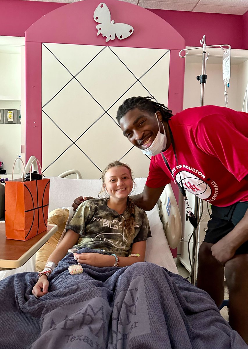 A team member from the University of Houston basketball smiles for a photo with a young patient sitting in a hospital bed at Children's Memorial Hermann Hospital.