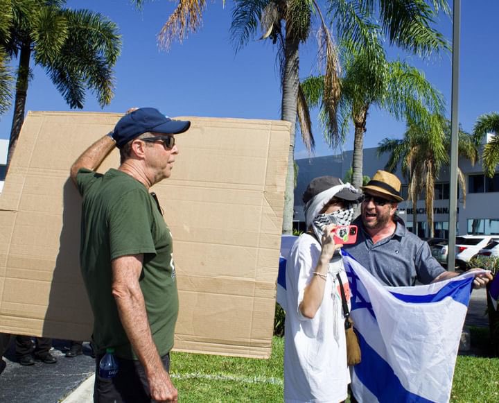 sdesfl's tweet photo. Alt text: 
Photo 1: “this is a genocide on the entire demography of Gaza” - Bisan Owda
Photo 2: end the genocide on cardboard 
Photo 3: cardboard that reads shut down real time labs stuck behind the back windshield wiper of a Boca PD police SUV
Photo 4: two ignore a yelling Zio https://t.co/3WVb6SuPbf