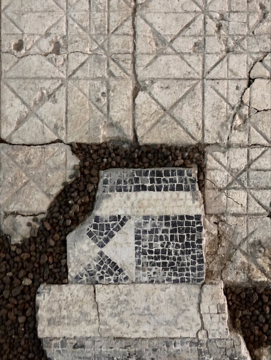 Black and white geometric mosaic fragment sitting atop a white lime preparation layer where the corresponding design has been scored into the surface.