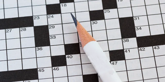 A close-up image of a crossword puzzle with a sharpened pencil resting on it.