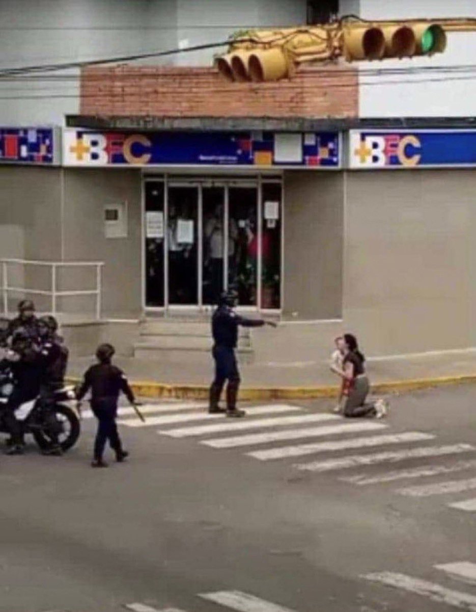 LeoKasura's tweet photo. 🚨🇻🇪 ABSURDO - Esta imagem deveria dar a volta ao mundo.

Um assassino de aluguel de Nicolás Maduro aponta uma arma de fogo para uma mãe venezuelana e seu filho ajoelhado no chão.

 Nicolás Maduro, você é um maldito tirano genocida! 

#VenezuelaLibre 
#VenezuelaLibreDelDictador https://t.co/AbQJcK2VQf
