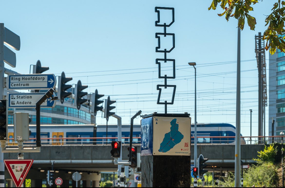 Zie hier verhalenpalen JJ17 naast Kastan

‘Hier is het druk, vliegtuigen, treinen, auto’s en overal hoogbouw. Ooit was het hier stil. Een weids landschap met lege akkers. De polder was strak verkaveld met een code voor iedere kavel. Dit is kavel JJ17’.