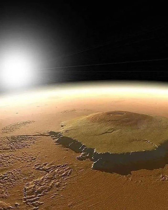 Rainmaker1973's tweet photo. Olympus Mons, located on Mars, is the second tallest mountain and largest volcano on any planet in the Solar System. It’s a shield volcano and it roughly covers an area of 300,000 km².

Due to the size and gentle slopes of Olympus Mons, an observer standing on the Martian surface would be unable to see its peak, because it'd be beyond the horizon. Similarly an observer near the summit wouldn't even see parts of Mars that aren't Olympus Mons.

[image: artist's impression]