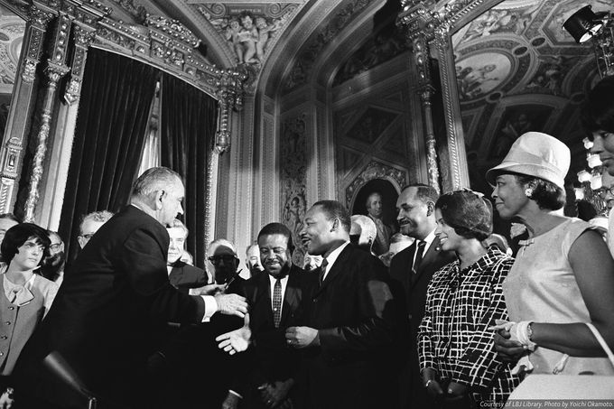 Black-and-white photograph of President Lyndon B. Johnson moving to shake hands with Martin Luther King, Jr. while others look on after signing the Voting Rights Act.