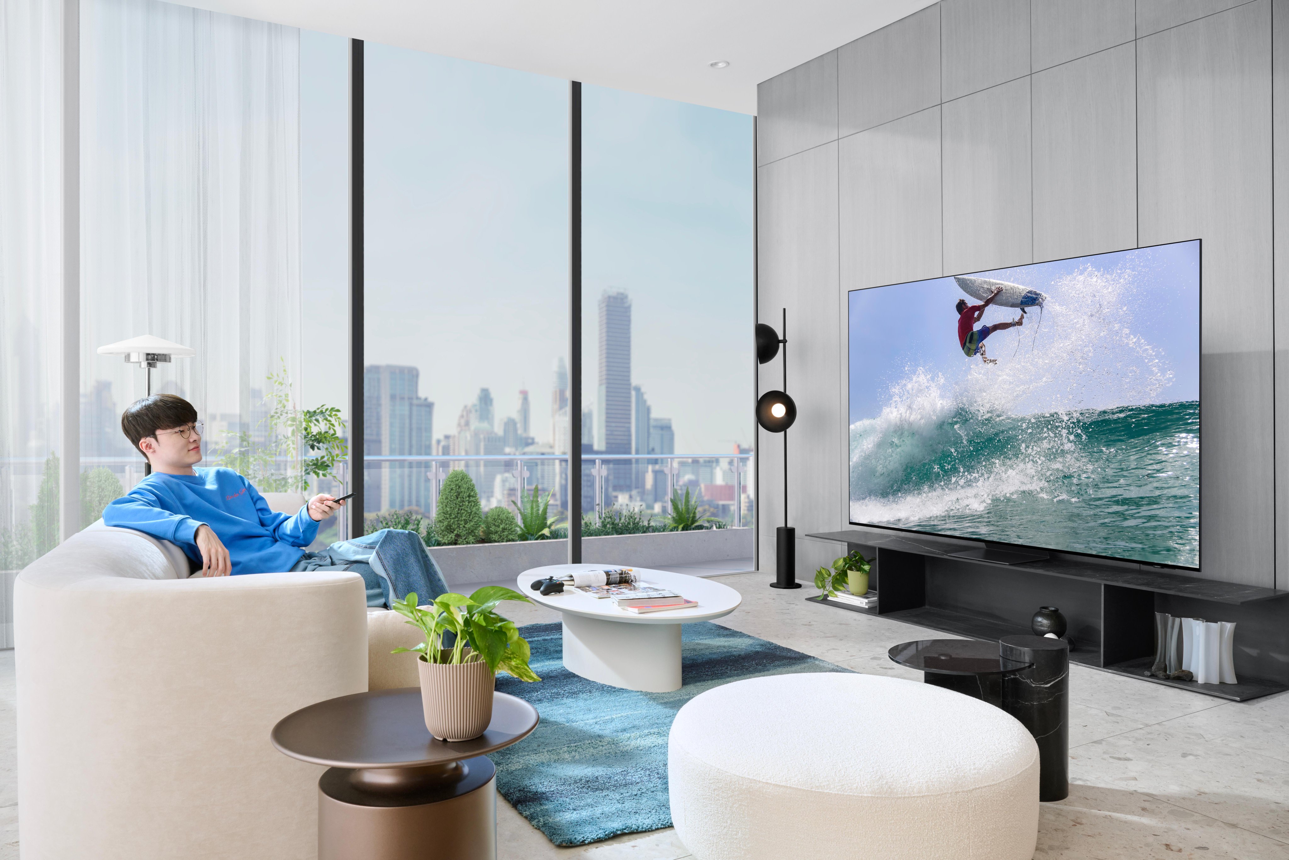 At the same room, team member Faker is holding a remote control and watching a surfer surfing through the waves.