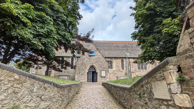 Image shows the entrance of the church with cobblestone walls and big wooden doors.