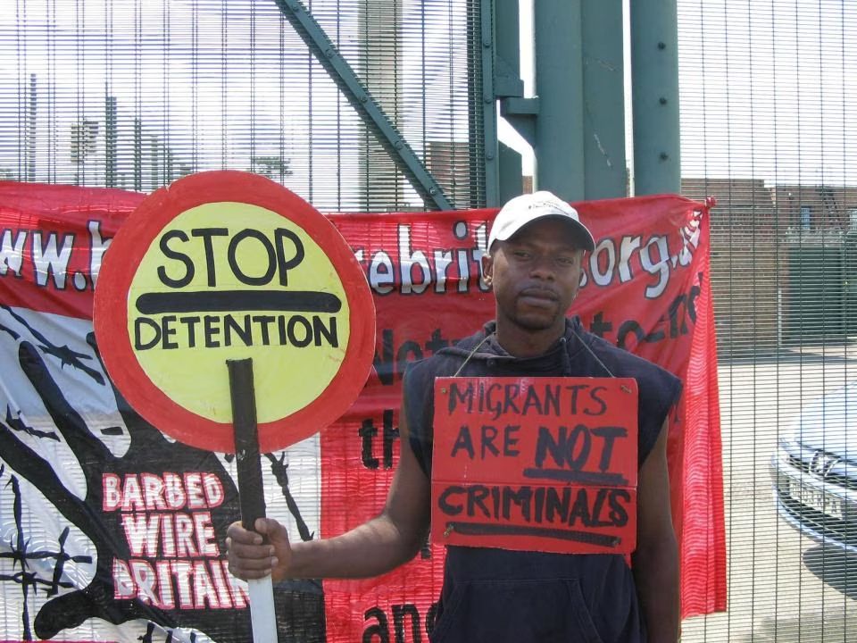 Steve_Laws_'s tweet photo. ‘Asylum seeker’ Anicet Mayela, charged with raping a 15-year-old girl, has had his court case adjourned due to “some administration delays”

He can be seen campaigning outside a detention centre holding a sign stating: “Migrants are not criminals”

He became a poster boy for anti-deportation campaigners after using human rights law to fight his return to the Republic of the Congo. 

Mayela has been fighting his return to the Republic of the Congo after arriving in the UK in 2004

20 YEARS HE HAS BEEN HERE PLAYING THE SYSTEM!

https://t.co/6vQHHltA6c