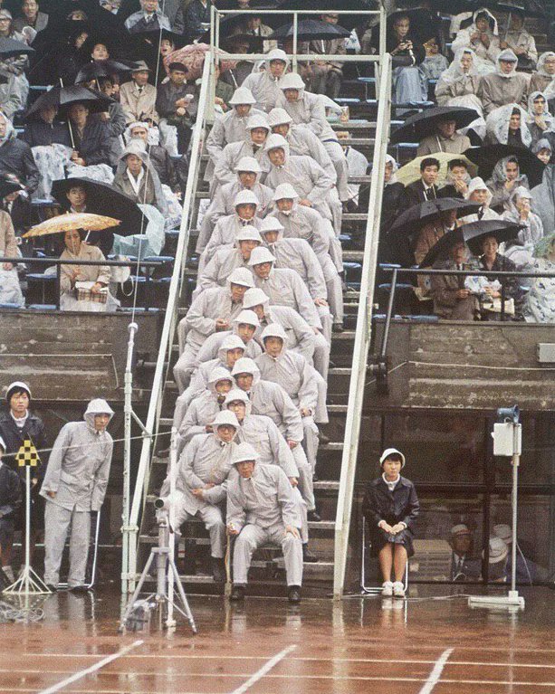 The 1964 Olympic Games in Tokyo.

People in white were observers at the running events. At that time, video recording was not yet used, and about 20 people would watch the finish line to track the runners.

Cameras were allowed to be used only 4 years later at the 1968 Olympics.