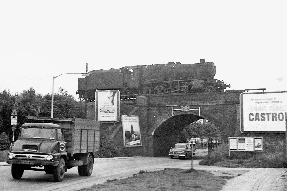 TrainStations23's tweet photo. Ex-LMS 8F 2-8-0 No 48713 runs light engine tender first over the A444 Nuneaton,  on it's way to pick up it's train in Abbey Street sidings, in early 1966.

Based at the former LNWR shed in Nuneaton, it has crossed under the West Coast Main Line by using the line connecting the turntable with the Leicester line. It has then reversed at Midland Junction and is now reversing back to Abbey Street sidings.

Photo by M S Lane