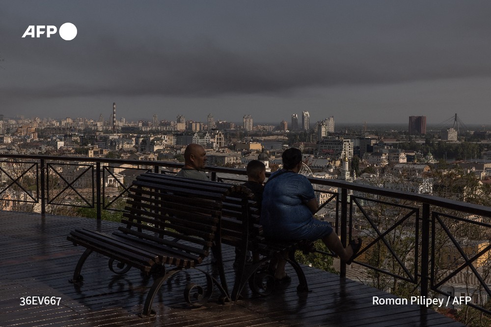 A man, a woman and a child look on as smoke rises over buildings in Kyiv, following a Russian air attack on August 26, 2024, amid the Russian invasion of Ukraine