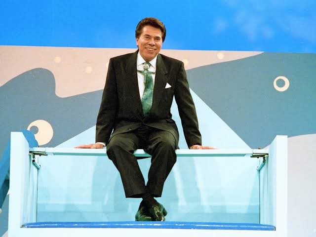 chicogarciaa's tweet photo. Eu estava vendo ao vivo neste dia. Quando o apresentador quebrou o protocolo e resolveu subir nesse tanque de água pra ver se era resistente. Caiu, arrancou gargalhadas e incredulidade. 

Foi o comentário geral na escola no dia seguinte.

Ele era único.

E assim como a mim, fez companhia a todo Brasil. Lembro de na infância e parte da adolescência, ficar na cama, com uma tevezinha de 10 polegadas, rindo e me divertindo com as pegadinhas, as brincadeiras e tudo que ele criou e construiu na televisão.

Li algumas vezes a sua biografia, já consumi sua história em seriados, filmes e sempre me espantei com a capacidade de um camelô se tornar o maior comunicador da história do país, além do empresário versátil e bem sucedido.

Outro momento que me marcou muito foi a revolucionária Casa dos Artistas. Numa época sem rede social, Silvio conversava com os participantes todos os domingos lendo as manchetes das revistas semanais com a repercussão do programa, o primeiro Reality show do Brasil.

Gênio.

Descanse em paz e obrigado por tudo.