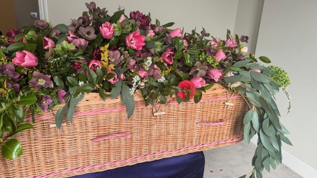 The beautiful handcrafted curved Somerset Willow Coffin with woven pink bands and handles, is adorned with a stunning spray of flowers carefully picked from the family’s garden. #Willow #Coffin #Floral #Handcrafted #Hurst