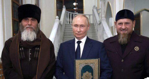 يبدو في هذه الصورة كالثعلب مخادع وبدعي حبه للاسلام وهو  يمسك بالقرآن الكريم. 
مع أنه هو أكثر من قتل من المسلمين ومجازره في سوريا تشهد على ذلك .كان طياروه يقصفون  المساجد حتى وهي مدمرة. وكانت تلغى صلاة الجمعة في المساجد بسبب القصف الروسي. هو يكذب والله أوقعه في شر  أعماله.