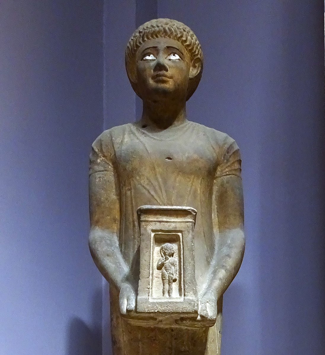 AwyanLehman's tweet image. The man is carrying a #Naos (shrine) with the image of #Horus as a child. The black stone irises were removed.

Picture taken at the Egyptian museum. Eroded marble from the Roman period, but copying a pose from the late dynastic period.