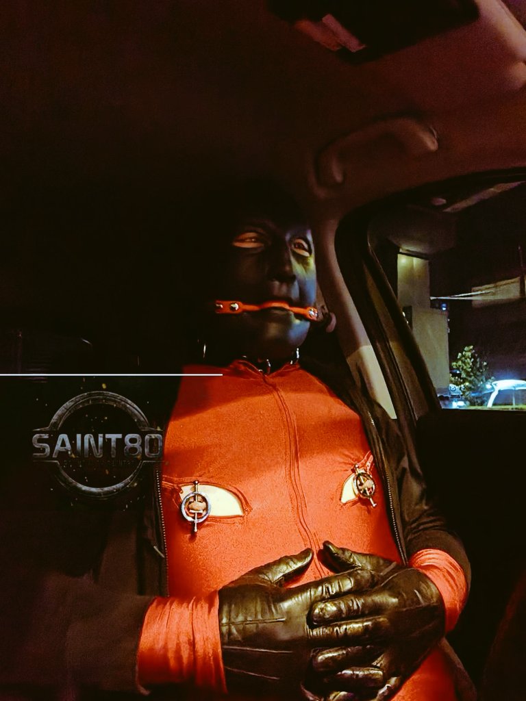 At the pick-up point, the car light flashes at me as I approach, and the boot opens automatically, revealing the trunks where I left the luggage. When I open the car door, I'm greeted by an unexpected sight—a boy, geared up in red, hooded and gagged, caged behind the wheels.