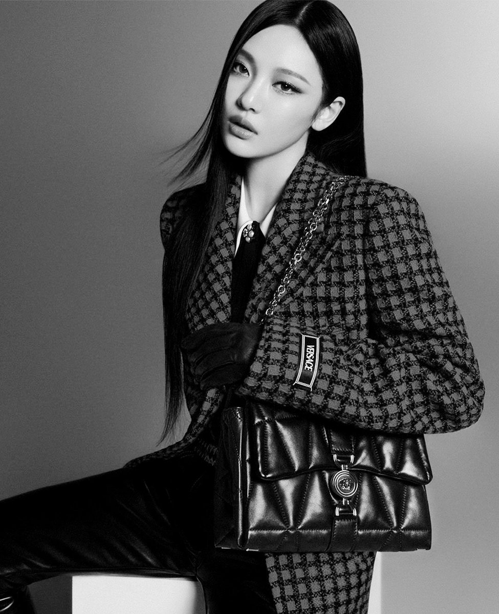 The minimalistic setting and the monochrome palette highlight the luxurious details of the attire and accessories, drawing attention to the refined fashion statement being made. The overall composition evokes a sense of timeless chic, with an emphasis on high fashion.