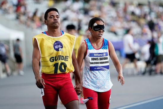 Ionis Dayana Salcedo, junto a su guía de competencia, se encuentran tomados de la mano en la pista de atletismo.