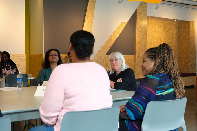 Senator Murray is sitting at the head of a table, with her arms crossed. She is smiling at a woman wearing a pink sweater who is seated with her back to the camera. There are two other women seated at the sides of the table on either side of the senator.