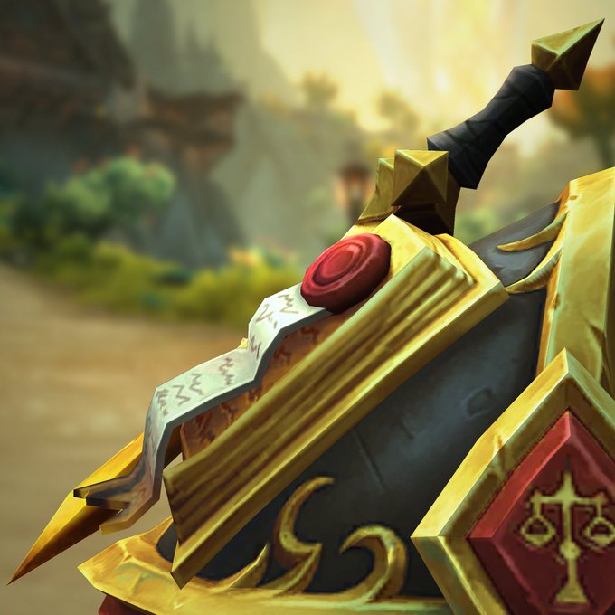 A close-up view of a single piece of shoulder armor, featuring a familiar golden book with small white scroll and red seal. A small golden sword is nested in the center of the open tome as it sits on black armor with gold trim. A red diamond-shaped emblem can be seen on the front of the piece, showing a gold balancing scale in its center. A blurred view of Hallowfall fills the background.