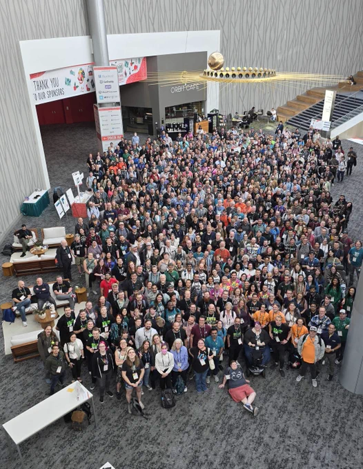 WordCamp US attendees posing for a large group photo, taken from the second floor of the convention center.