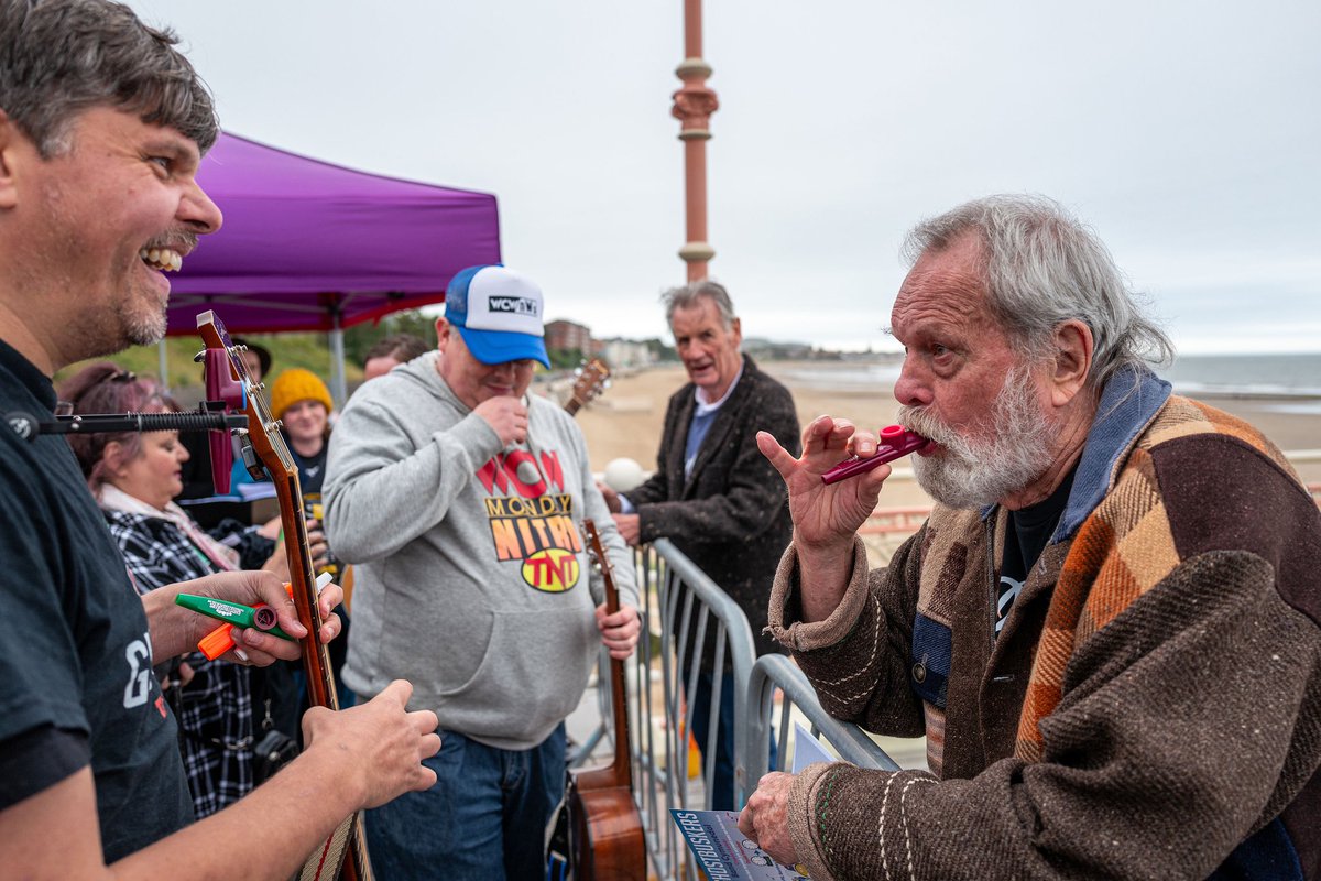PythonJones's tweet image. Mike watches on as Terry G learns the kazoo at A Python on the Prom launch day in Colwyn Bay. The wonderful @GhostbuskersO serenaded us with their specially written song about Terry J. Click here to donate to a statue of Terry Jones gofundme.com/terryjonesstat…  📷©️Paul Sampson