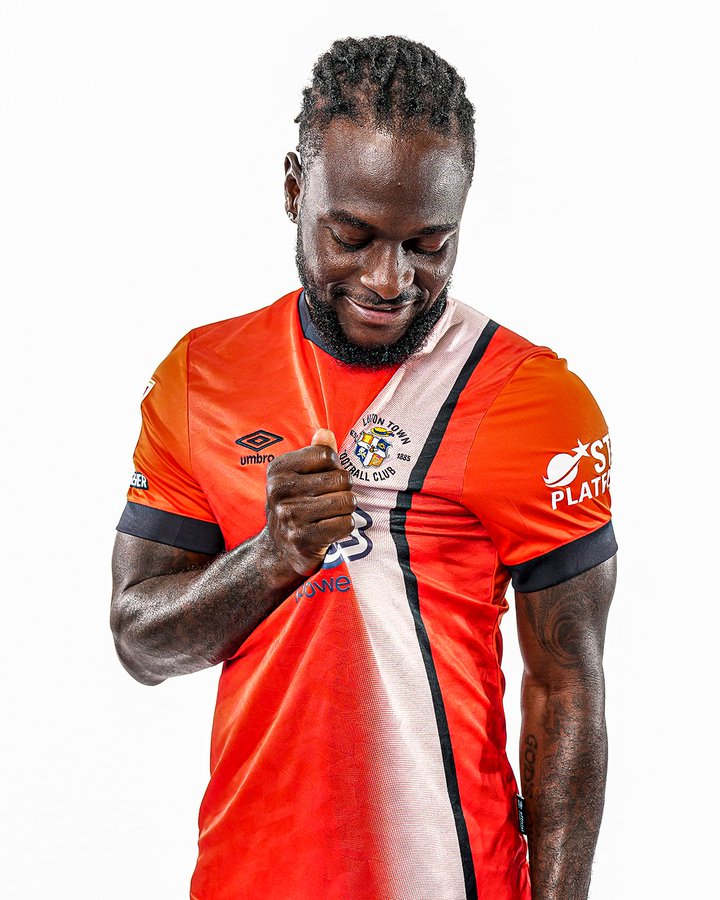 Victor Moses pulling on the Luton Town badge on his shirt and looking at it.