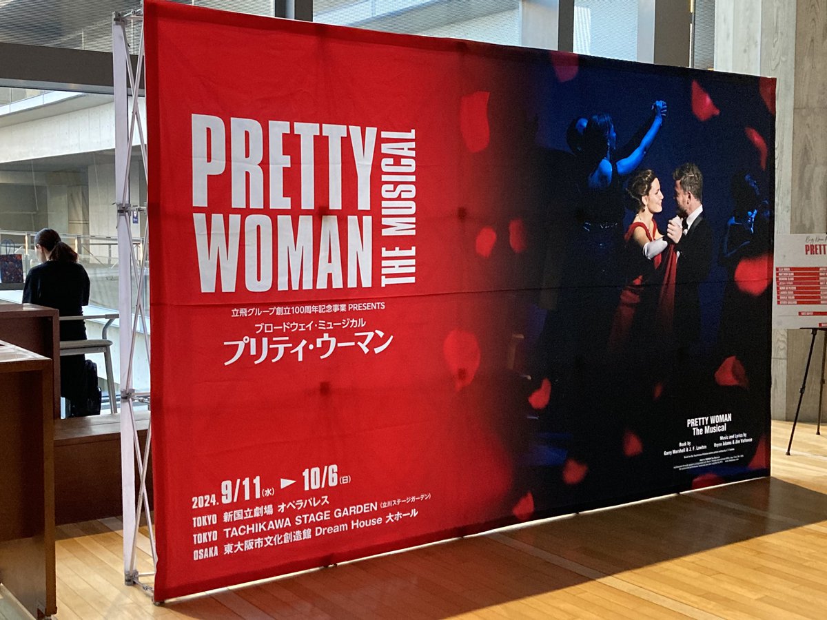 ミュージカル『プリティウーマン』
劇場のフォトスポットに設置された大きな幕。
横長の左半分には、赤い背景に大きくタイトルロゴ。
右半分にはダンスを踊るドレスアップしたヴィヴィアンとエドワード。
周りに薔薇の花びらが舞っている。