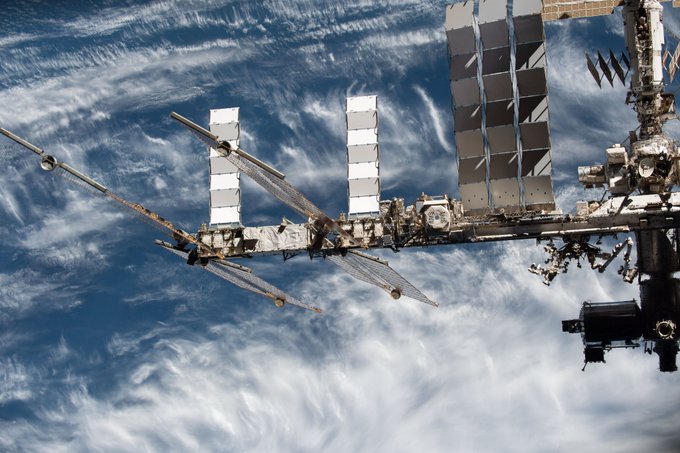 iss066e079533 --- A truss of the space station extends from the right across the center of this image. Several modules of the station are visible on the right. From right to left are a large solar panel extending toward the top of the image, and next to it, the hexagonal top of AMS-02 is visible. Two additional solar panels extend toward the top of the image and two others to either side of the truss. In the background is the blue Earth with scattered white clouds.