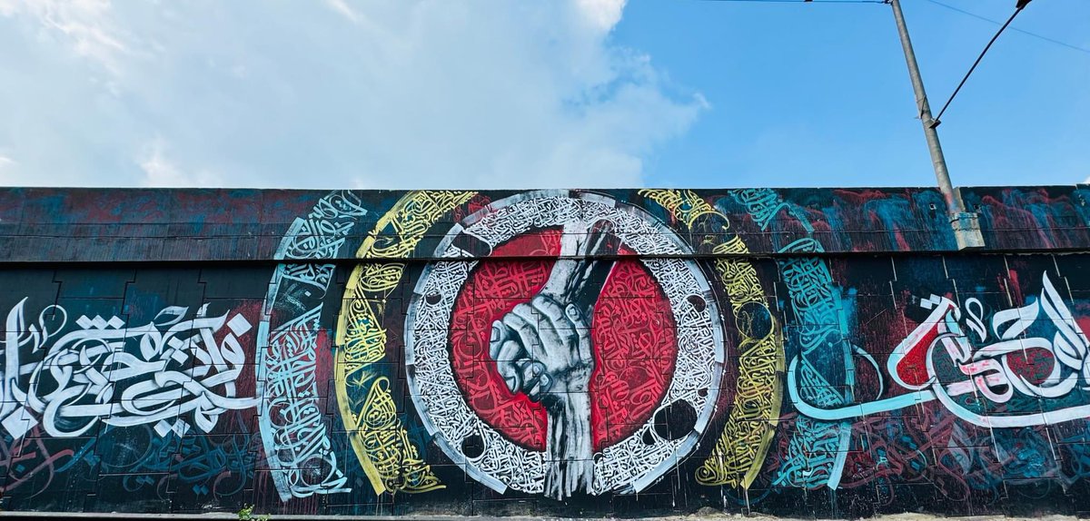 ridoanmahbub's tweet photo. Bangladesh's largest graffiti artwork has transformed the walls of Kachpur in Narayanganj into a breathtaking urban canvas. This vibrant mural features intricate Arabic calligraphy framing a powerful central image of one hand helping another, symbolizing unity and support. This public art, set against the backdrop of daily life, has quickly become an iconic landmark, capturing the attention of both locals and visitors.