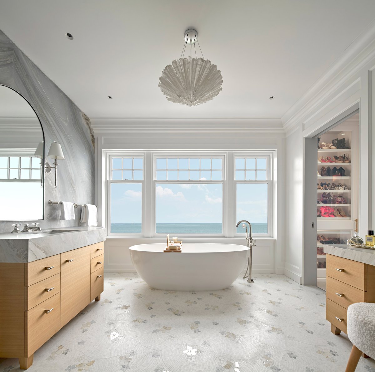 Our award-winning Contemporary Shingle’s primary bathroom features book-matching marble walls, exposed free-standing shower plumbing, modern white oak vanities with matching marble tops, and an inviting freestanding soaking tub with breathtaking water views.⁣⁣ #luxuryhomes