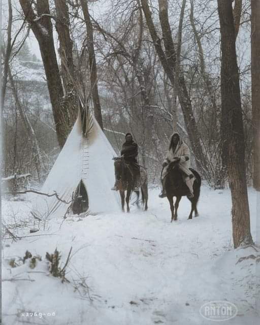 Two Apsaroke Native Americans on horseback outside of a tipi in a snow-covered forest in Montana in 1908..