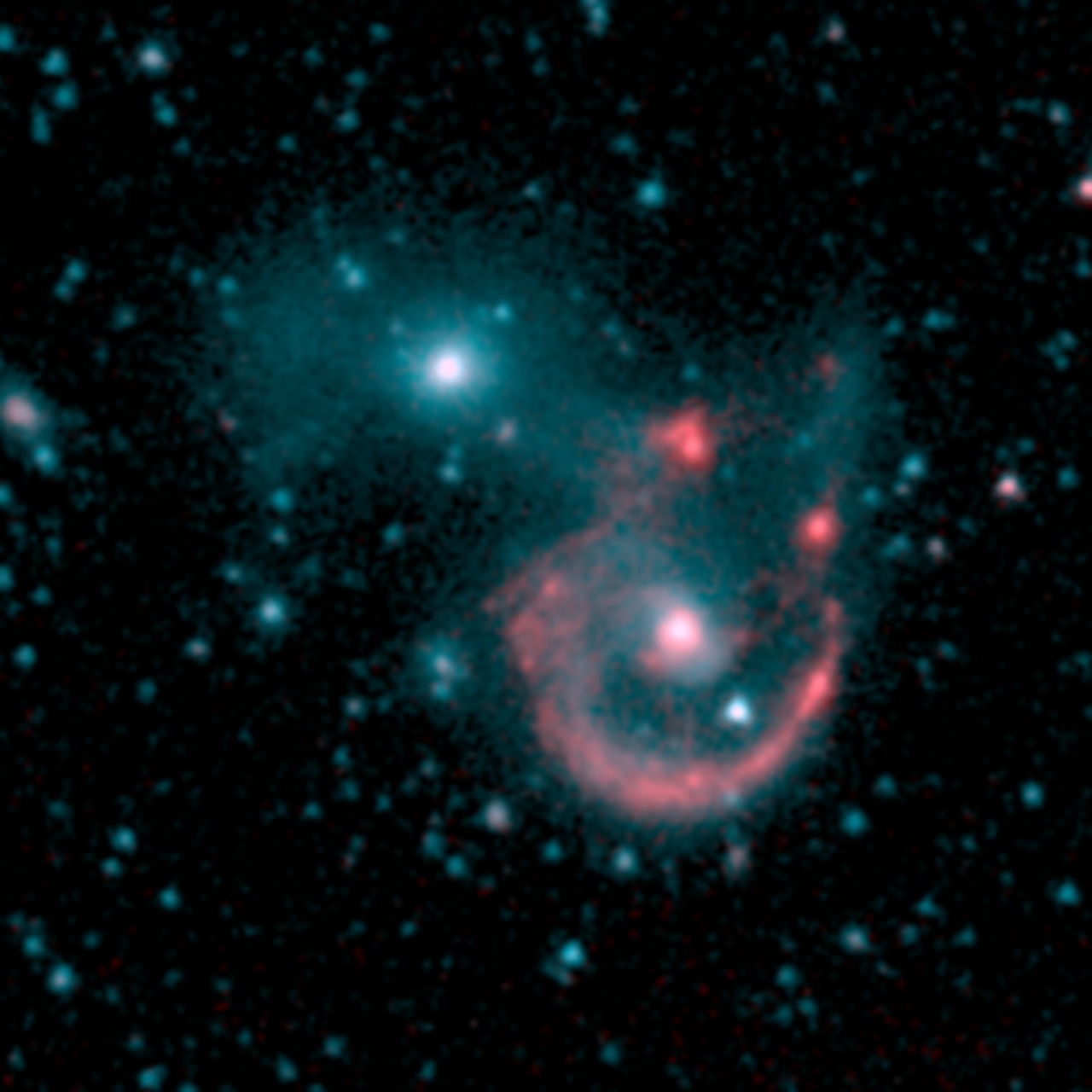 Spitzer’s infrared image is more diffused than either Hubble or Webb. Just right of center is a bright red dot, which is the center of the spiral galaxy. It is surrounded by a reddish ring, which are the galaxy’s arms. The gap (here at top right) is bordered by two reddish pockets of dust and gas. The smaller galaxy is at top left. It’s a bright blue dot surrounded by light blue haze. Background galaxies and stars are hazy blue dots. 