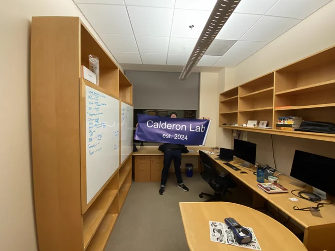 Unraveling a giant poster that says "Calderon Lab est. 2024"