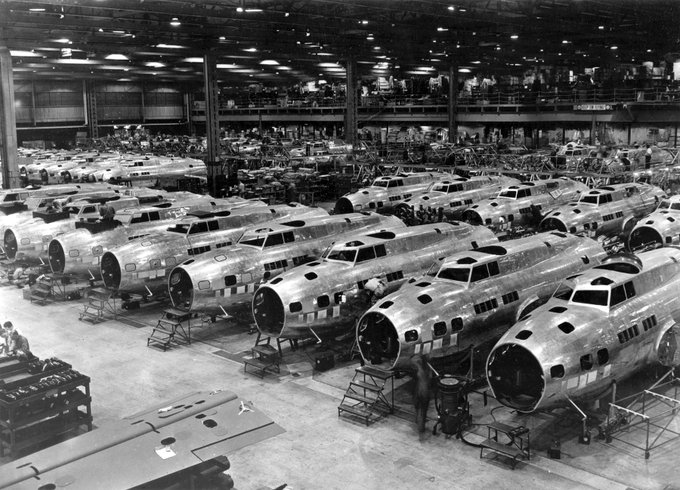 Black and white photo of an assembly line at a Boeing factory with multiple airplanes in various stages of construction.