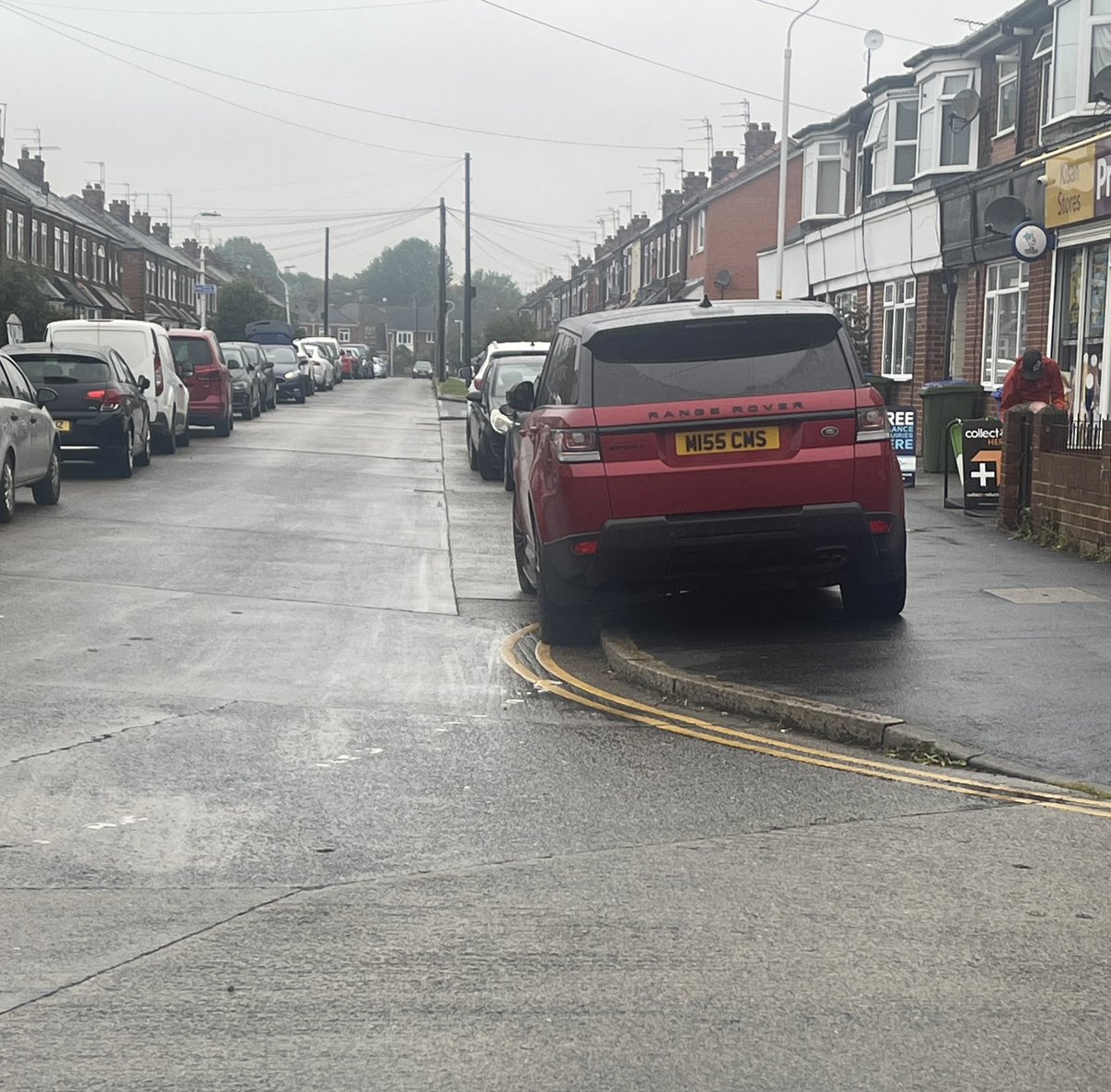 dgarnett's tweet photo. Another day. This time in the wet weather. More cars. Flying down dodging badly parked cars and kids. Woman in white car engine running playing on her phone while blocking drop curb for crossing. https://t.co/h2OCT9KCPl