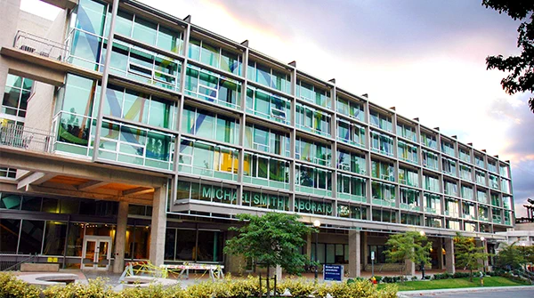 An exterior shot of the Michael Smith Laboratories building. A distinguishing feature of the building, a DNA helix is pictured across the large front-facing windows.