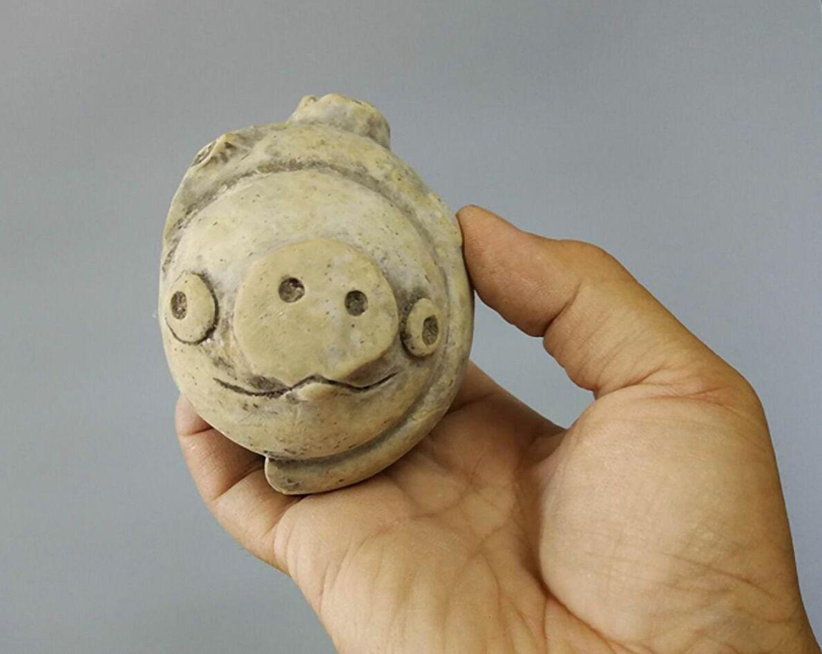Clay Pig Figurine, approximately 3,000 years old, excavated in 2020 from the Lianhe Ruins, China. This small, rounded figure represents a pig, created using local clay. Its simplistic facial features, which have drawn comparisons to modern cartoon depictions, are reminiscent of
