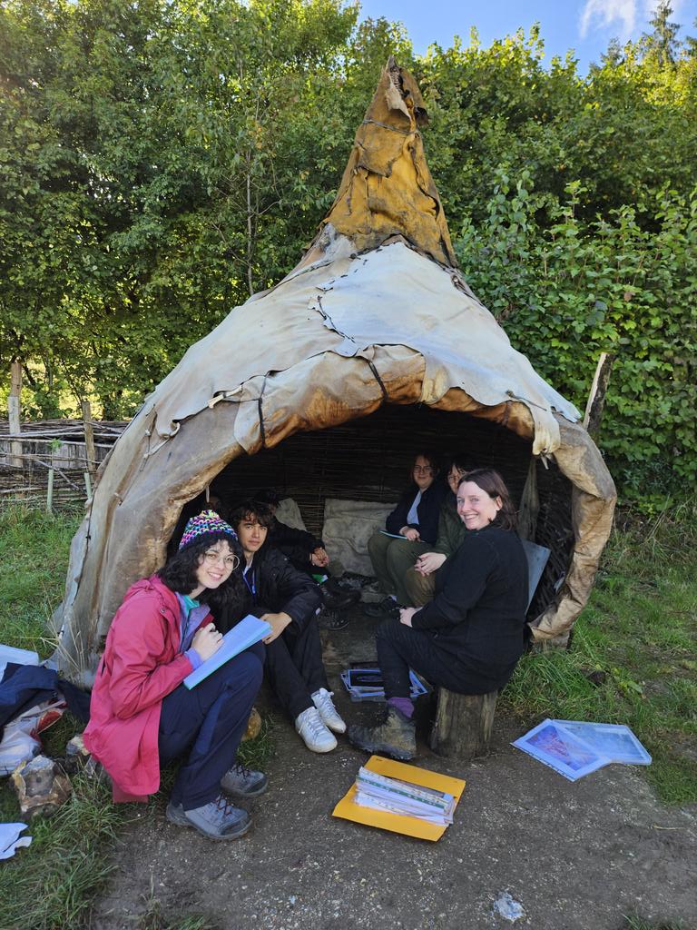 MatthewPope's tweet photo. How is thos for a classroom. One of @butserfarm's Mesolithic period structures, and in it @LettyIngrey teaching stone age art to our first year students.
#Atech24 https://t.co/pShy2lbwbR