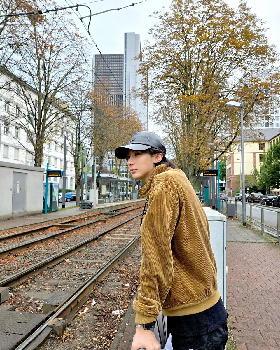 The cool autumn air surrounds me as I stand by the tracks, my corduroy jacket blending with the warm tones of the fallen leaves. The peaceful streets and towering trees make this quiet moment feel just right.