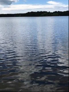 Pictured is a pond with partly cloudy and blue sky reflected in the water.