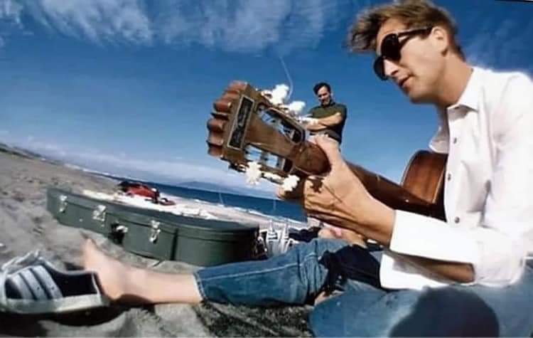Weet iemand wie hier met zijn vintage sneakers op het strand gitaar aan het spelen is? Hij is trouwens jarig vandaag