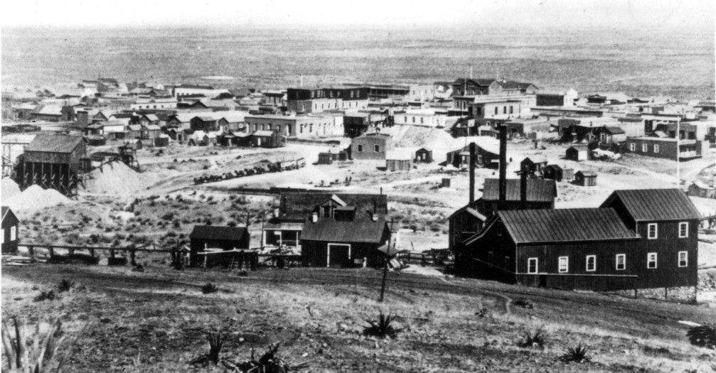 Tombstone, Arizona in 1881 photographed by C. S. Fly. An ore wagon at the center of the image is pulled by 15 or 16 mules leaving town for one of the mines or on the way to a mill. The town had a population of about 4,000 that year with 600 dwellings and two church buildings.