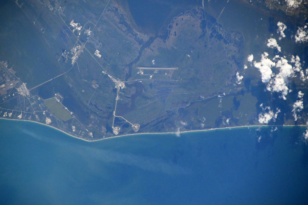 Astro_ChrisW's tweet image. I took this photo of @NASAKennedy this weekend. It is not my best photo (should have grabbed a different lens) but it is special – if you zoom in on the rightmost launch pad, you can see a shadow just to the left of the center of the pad. That shadow is from the rocket (and…
